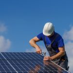 A man worker installing solar photovoltaic panels on roof, alternative energy concept.